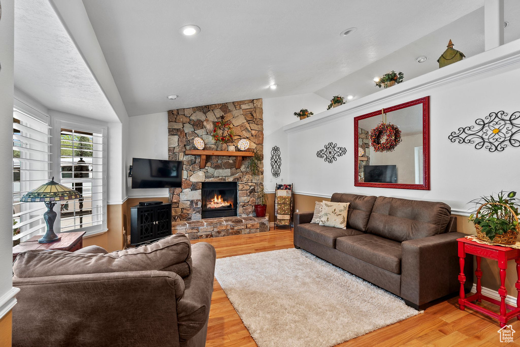 Living room featuring vaulted ceiling, a stone fireplace, and light wood finished floors