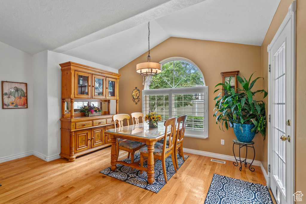 Dining space with vaulted ceiling, light wood-style flooring, baseboards, and a chandelier