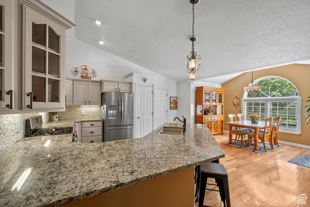 Kitchen with appliances with stainless steel finishes, a sink, vaulted ceiling, tasteful backsplash, and light stone counters