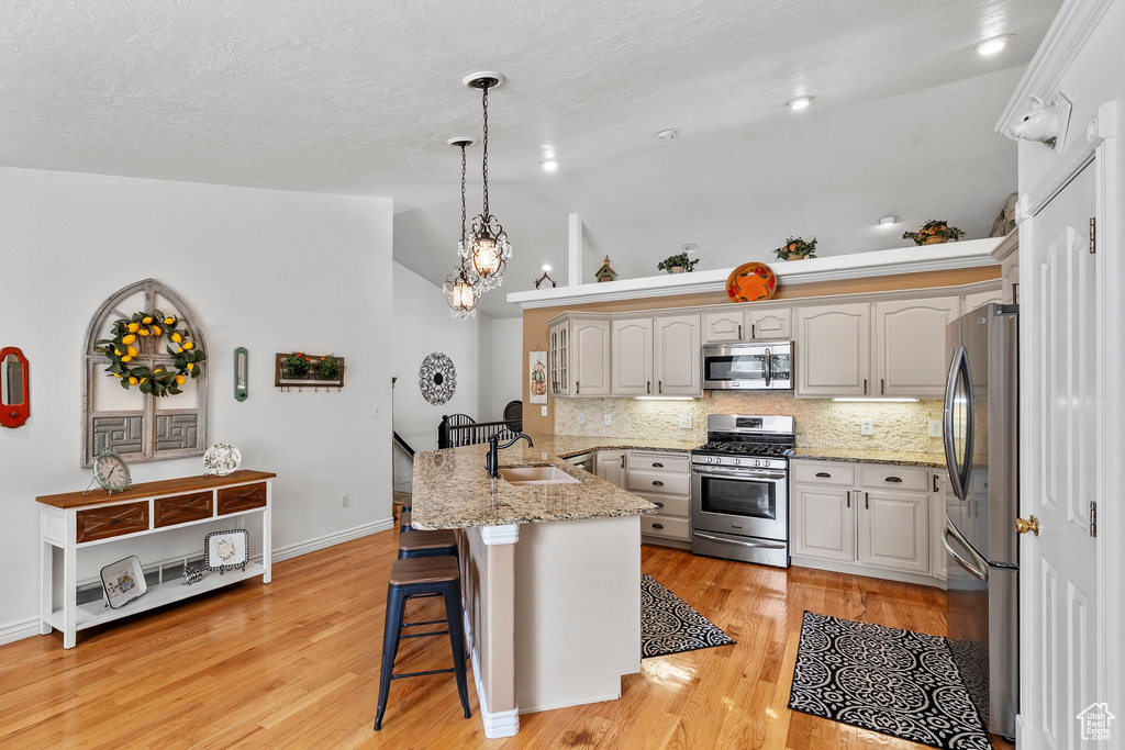 Kitchen featuring appliances with stainless steel finishes, a peninsula, a breakfast bar area, vaulted ceiling, and backsplash