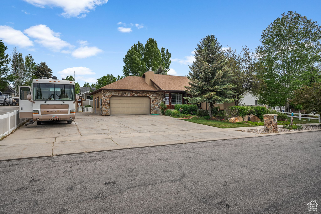 View of front of property featuring a garage, stone siding, driveway, and a chimney