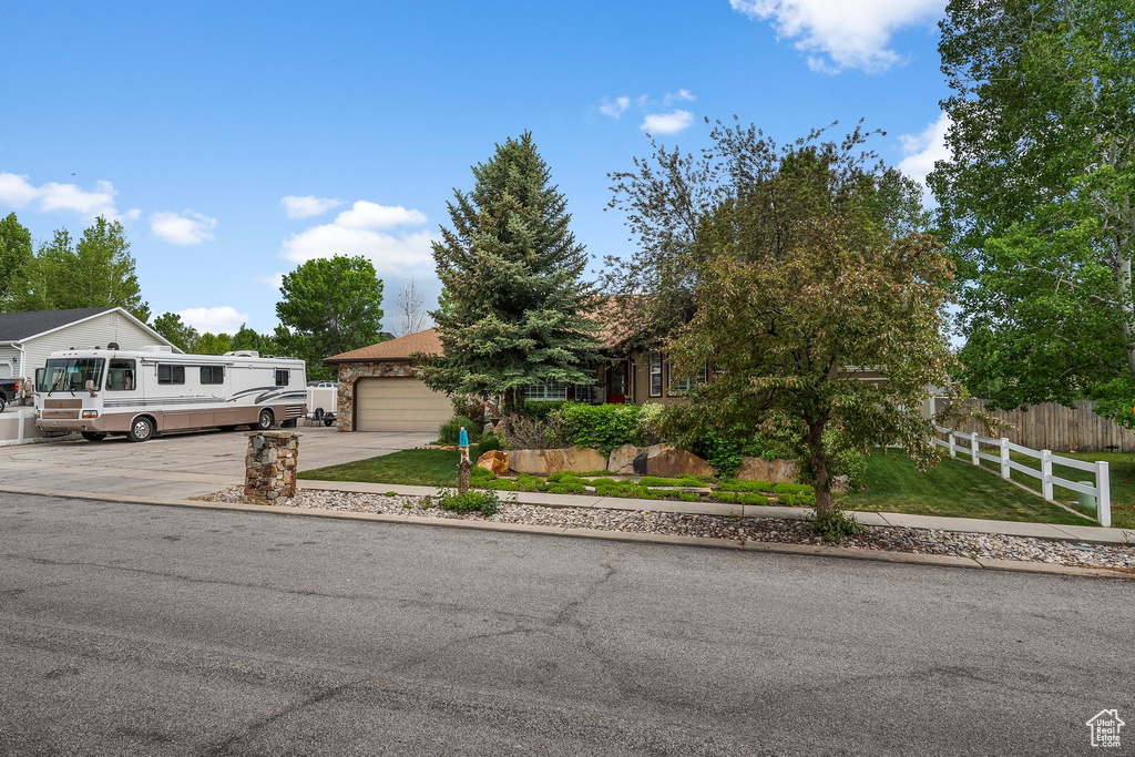 View of property hidden behind natural elements featuring concrete driveway and a garage