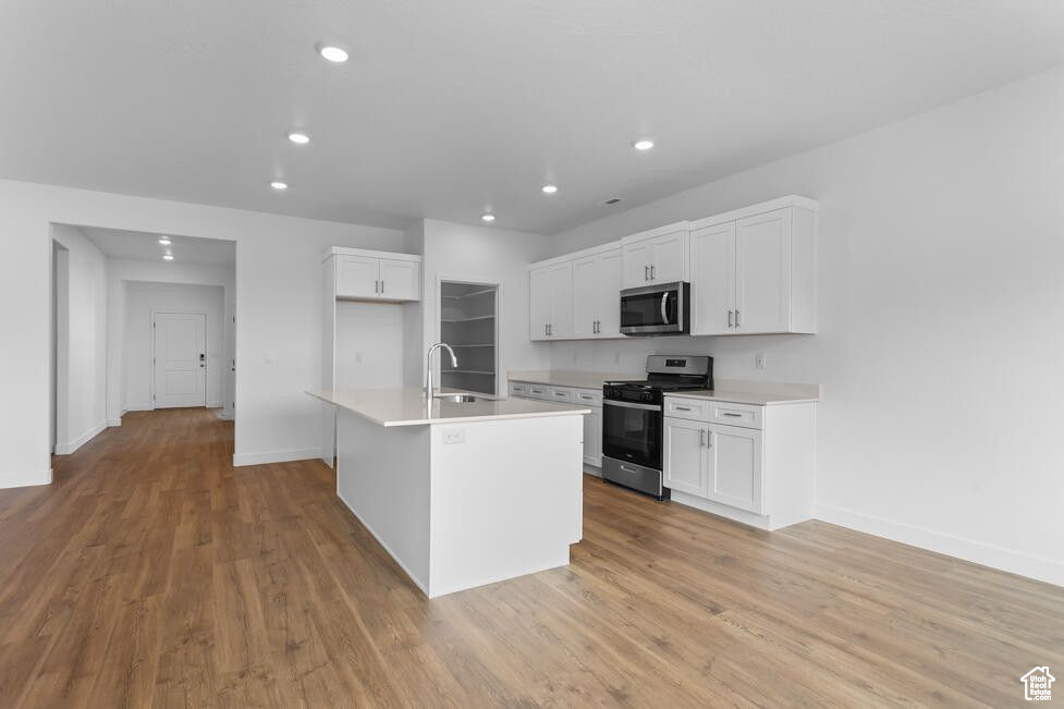 Kitchen featuring stainless steel appliances, a sink, baseboards, recessed lighting, and white cabinetry