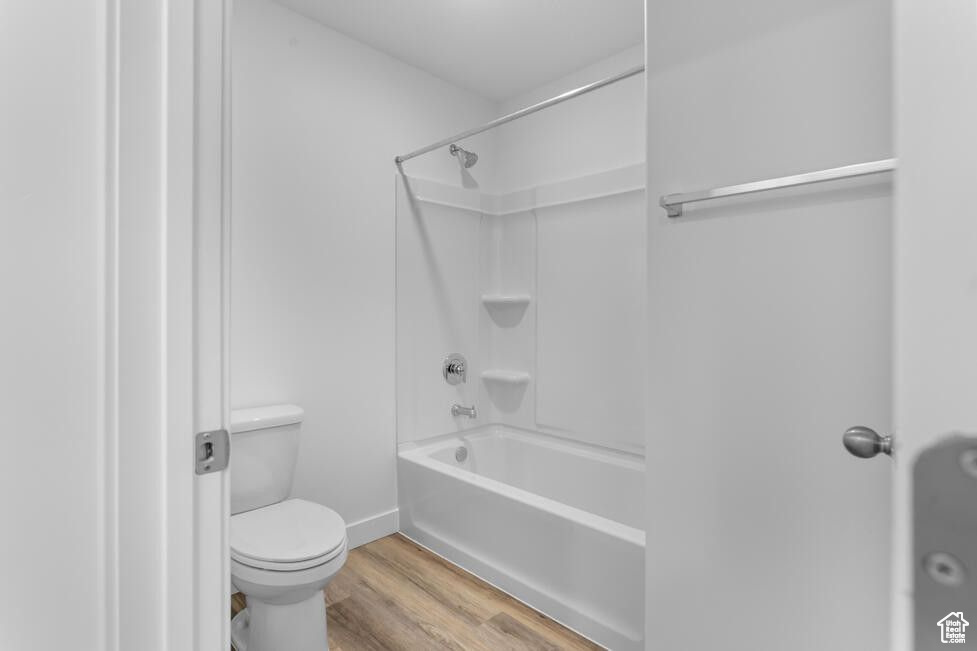 Full bath featuring wood finished floors, toilet, shower / washtub combination, and baseboards