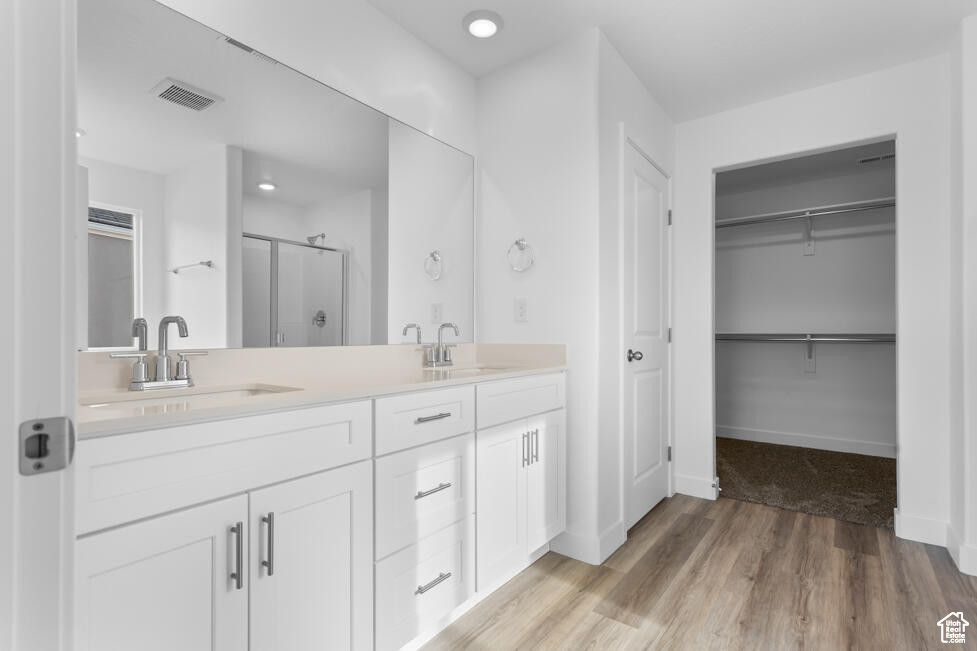 Bathroom featuring a shower stall, double vanity, wood finished floors, a walk in closet, and baseboards