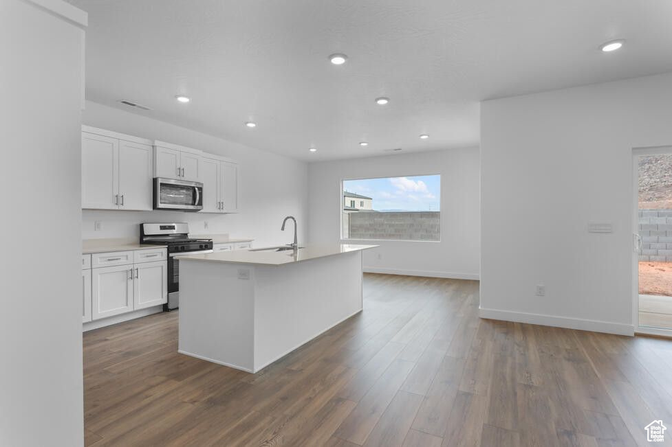 Kitchen with appliances with stainless steel finishes, a sink, white cabinets, a center island with sink, and dark wood-style flooring