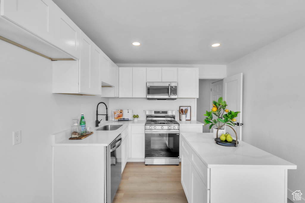 Kitchen with stainless steel appliances, a sink, recessed lighting, white cabinetry, and a kitchen island