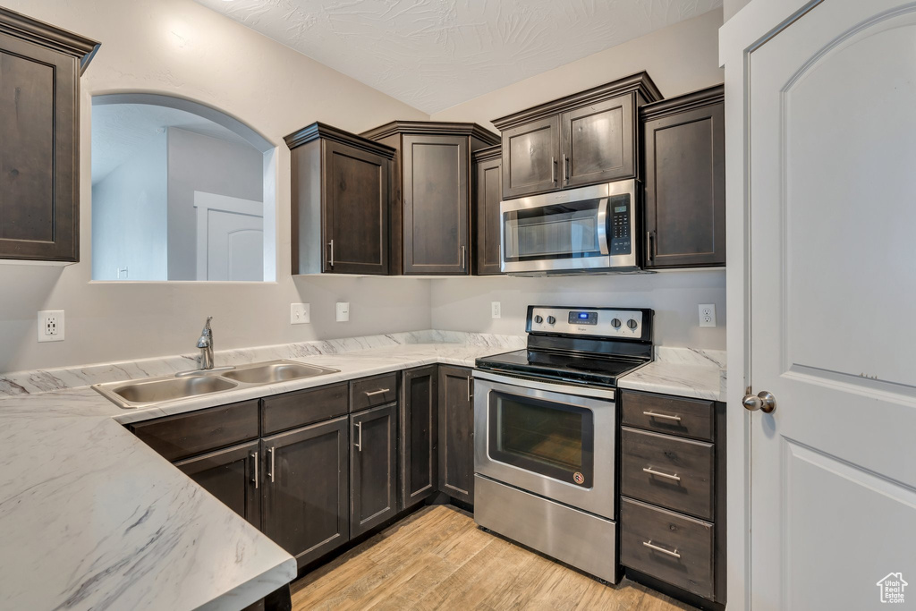 Kitchen featuring appliances with stainless steel finishes, a sink, light wood finished floors, dark brown cabinets, and arched walkways