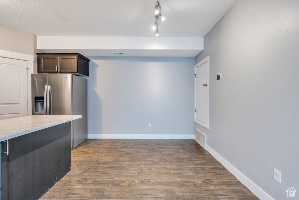Kitchen with stainless steel fridge, dark brown cabinets, wood finished floors, and light stone counters