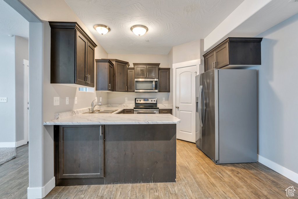 Kitchen with appliances with stainless steel finishes, a sink, dark brown cabinets, baseboards, and a peninsula