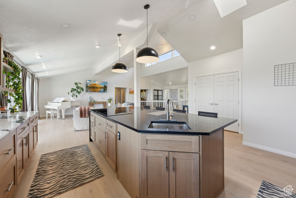 Kitchen with a sink, light wood finished floors, vaulted ceiling, baseboards, and a kitchen island with sink