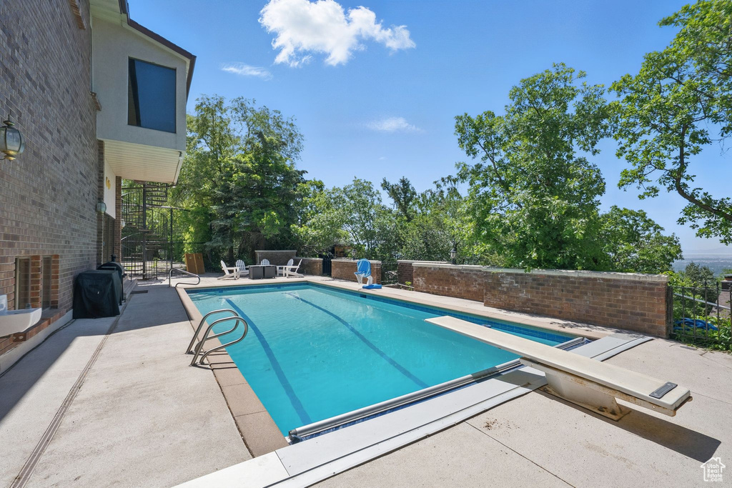 View of pool with a patio area and a diving board