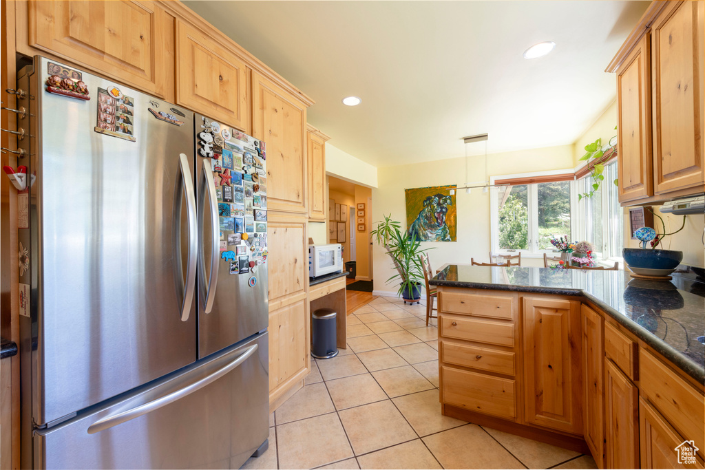 Kitchen featuring freestanding refrigerator, white microwave, light tile patterned floors, a peninsula, and dark stone countertops