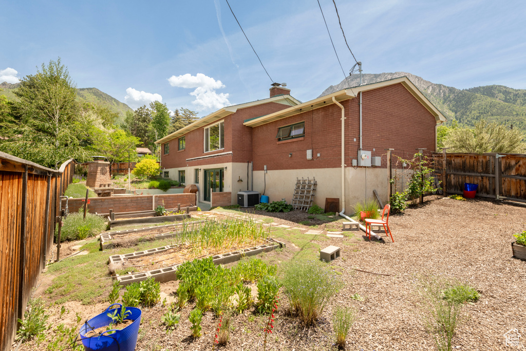 Back of house featuring a vegetable garden, brick siding, a mountain view, central air condition unit, and a chimney