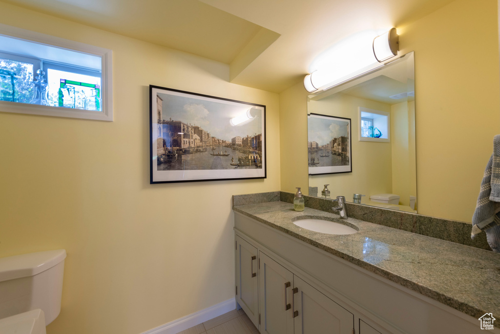 Half bathroom with toilet, plenty of natural light, vanity, and baseboards