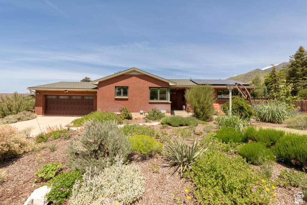 Ranch-style home with brick siding, a garage, roof mounted solar panels, and driveway