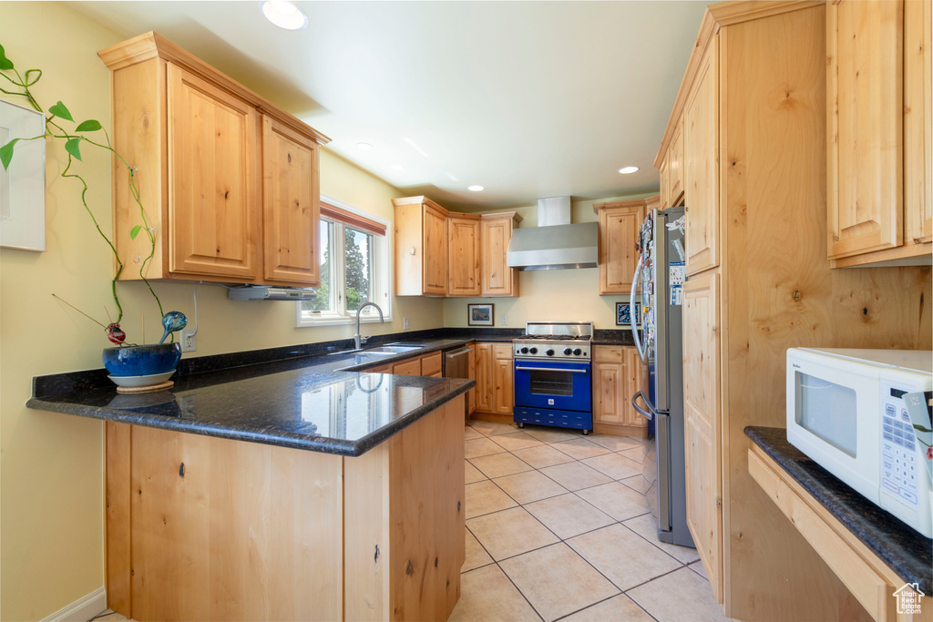 Kitchen with stainless steel appliances, wall chimney exhaust hood, a peninsula, a sink, and light brown cabinetry