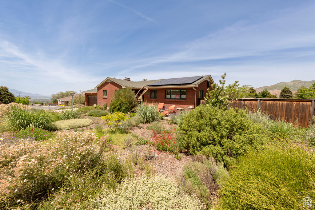 Back of house with brick siding, roof mounted solar panels, a mountain view, and a chimney