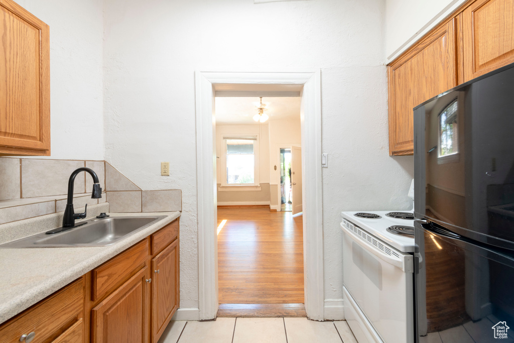 Kitchen with freestanding refrigerator, white electric stove, a sink, light countertops, and baseboards