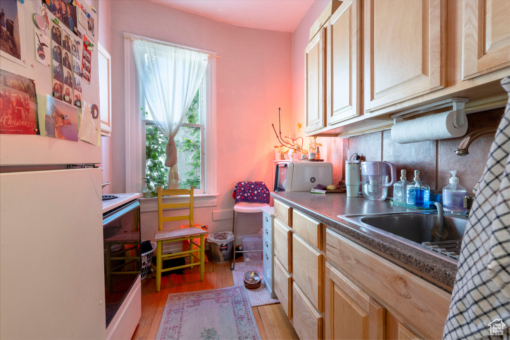 Kitchen featuring white appliances, light wood-type flooring, light brown cabinets, and decorative backsplash