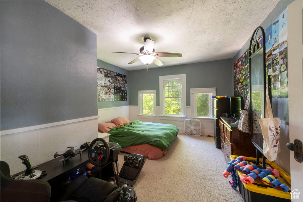 Carpeted bedroom featuring a textured ceiling, ceiling fan, and a wainscoted wall