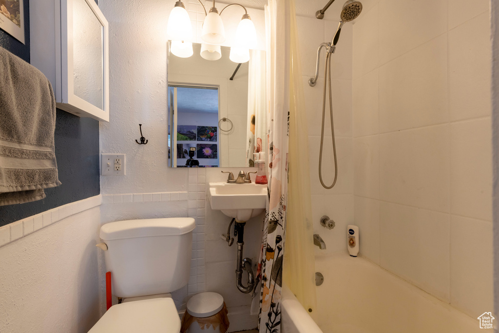 Bathroom featuring shower / tub combo with curtain, toilet, wainscoting, and tile walls