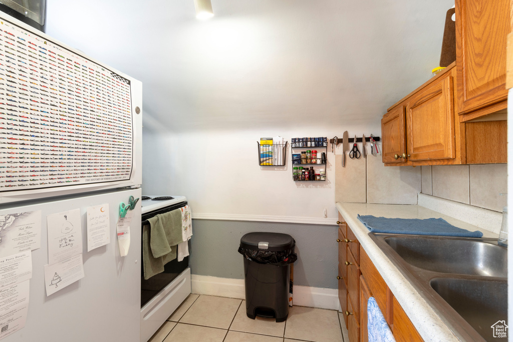 Kitchen featuring white range with electric stovetop, light countertops, brown cabinetry, light tile patterned flooring, and refrigerator