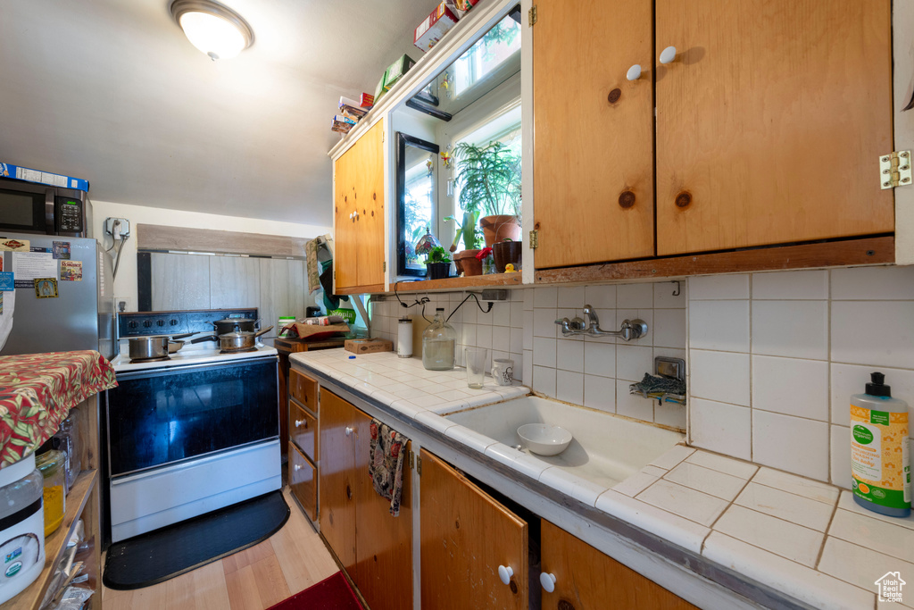 Kitchen featuring tile counters, white range with electric stovetop, backsplash, and a sink