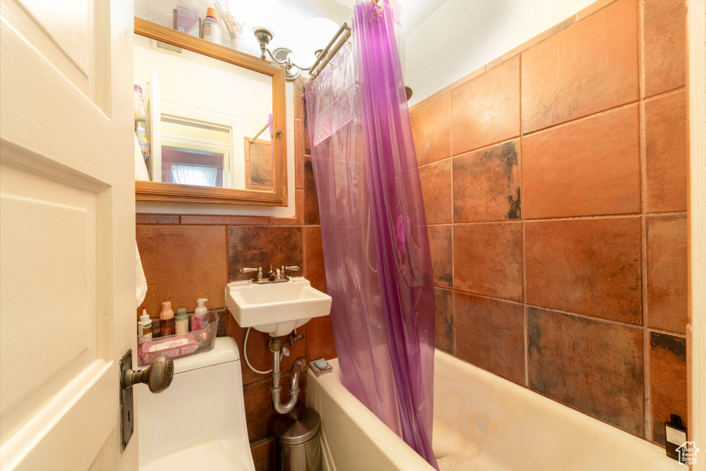 Bathroom with tile walls, shower / bathtub combination with curtain, toilet, and a sink