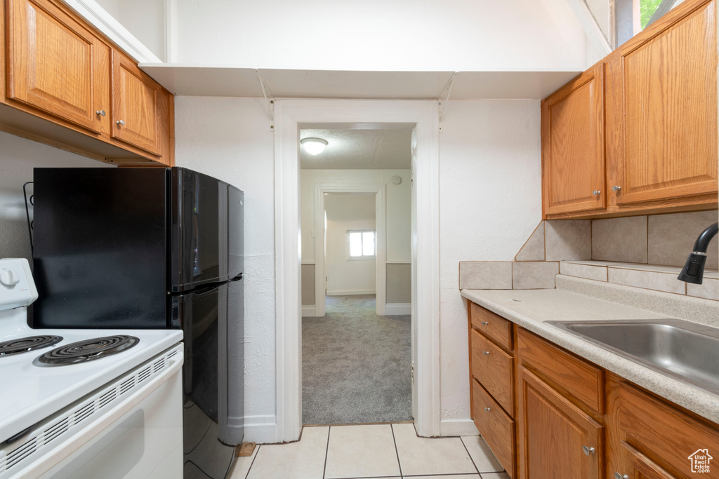 Kitchen with white electric range oven, a sink, light carpet, tasteful backsplash, and light countertops