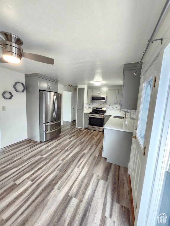 Kitchen with stainless steel appliances, gray cabinets, wood finished floors, and light countertops