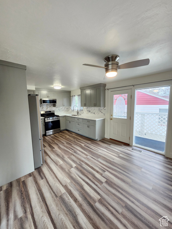 Kitchen featuring stainless steel appliances, gray cabinets, a sink, light wood-type flooring, and a ceiling fan
