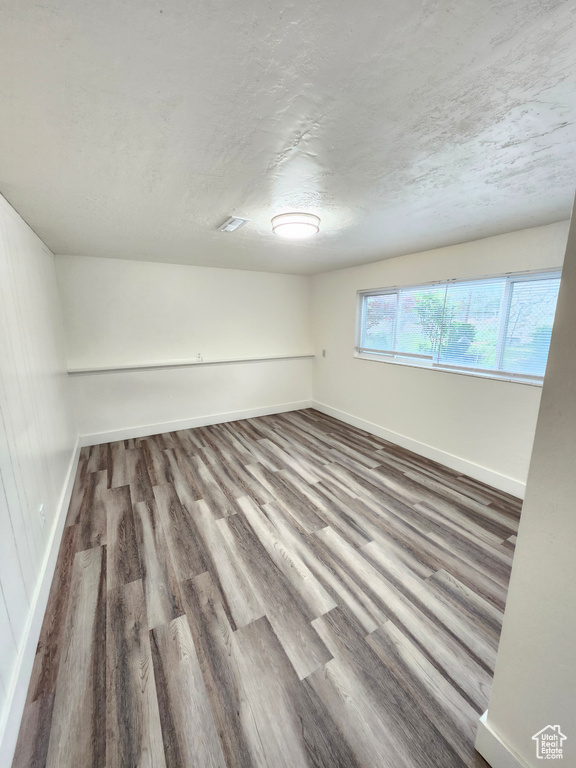 Unfurnished room featuring baseboards, wood finished floors, and a textured ceiling