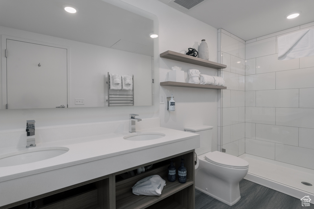 Bathroom featuring toilet, double vanity, a tile shower, wood finished floors, and recessed lighting