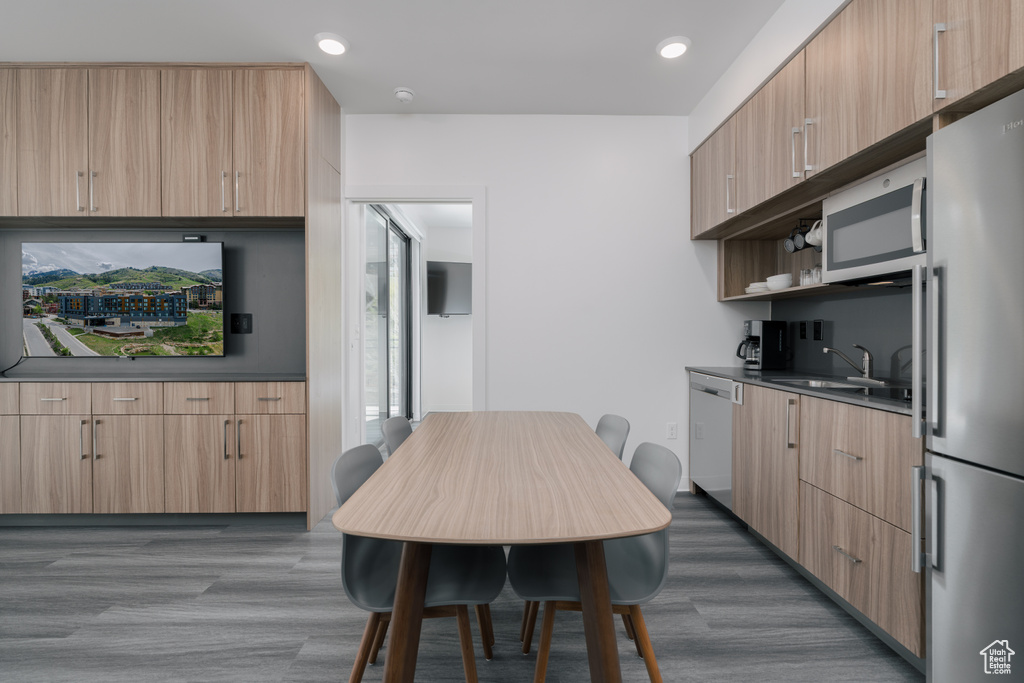 Kitchen featuring appliances with stainless steel finishes, a sink, dark wood-style floors, dark countertops, and light brown cabinets