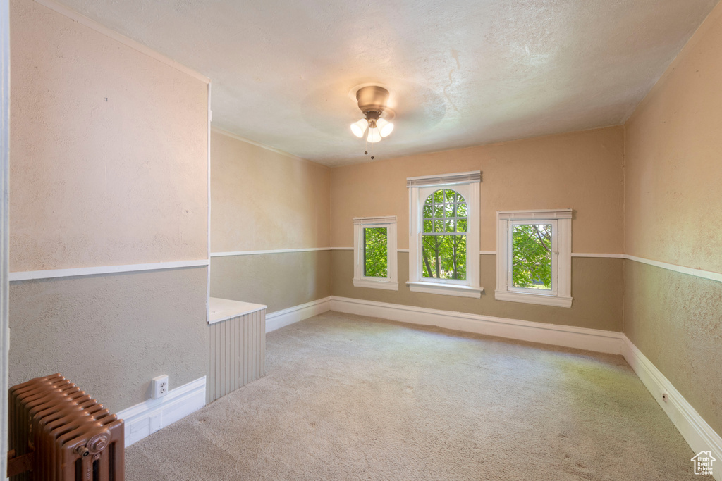 Spare room with radiator heating unit, carpet floors, baseboards, and a textured wall
