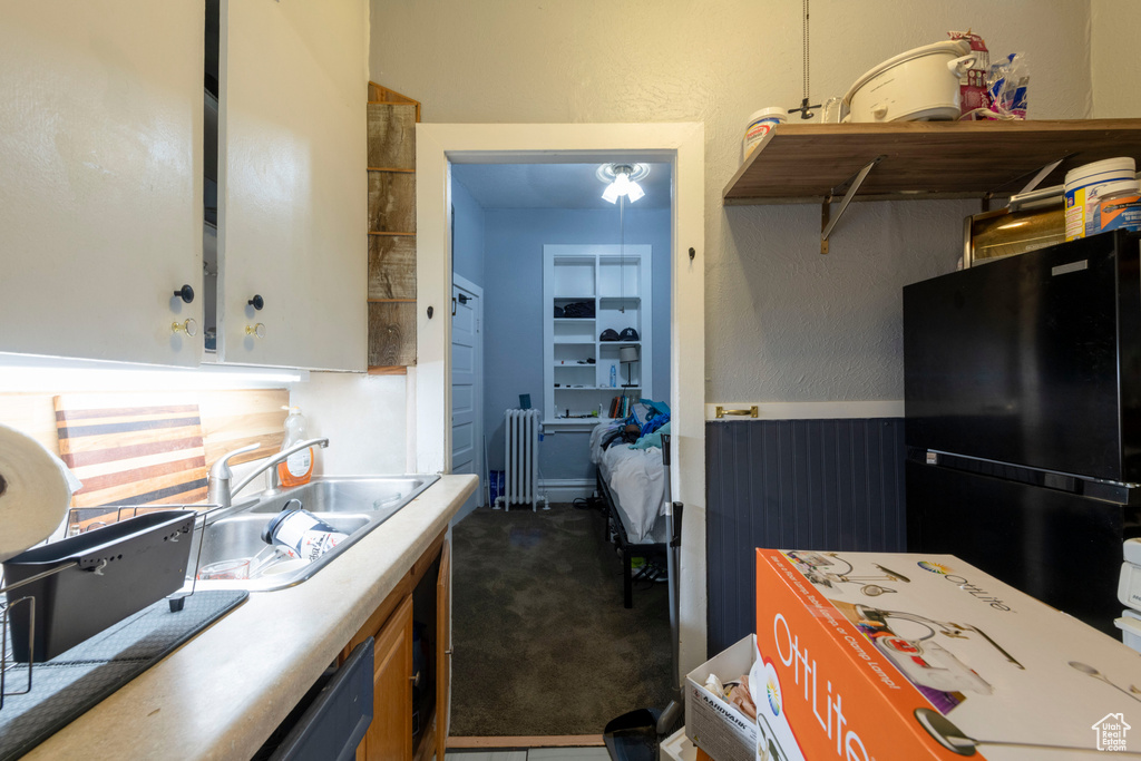 Kitchen with freestanding refrigerator, radiator heating unit, dark carpet, a sink, and light countertops