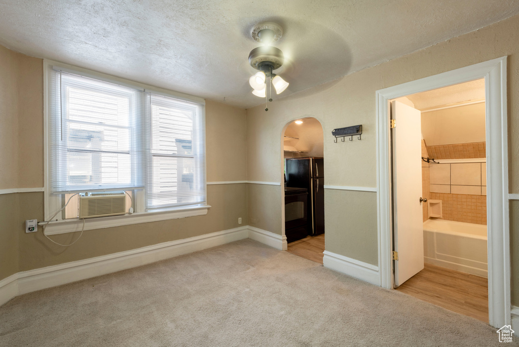 Empty room featuring light colored carpet, ceiling fan, arched walkways, baseboards, and a textured ceiling