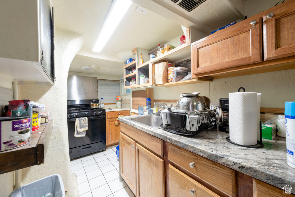 Kitchen featuring black gas range oven, light tile patterned floors, a sink, light countertops, and open shelves