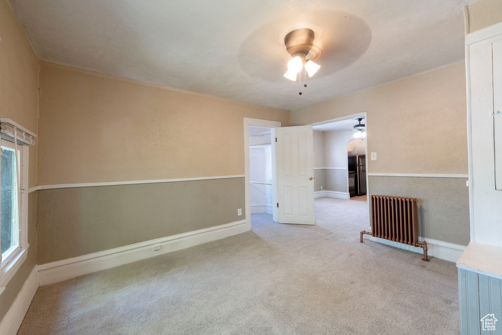 Spare room with ceiling fan, radiator heating unit, carpet flooring, and baseboards