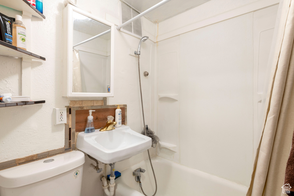 Full bathroom with shower / bath combo with shower curtain, toilet, a sink, and a textured wall