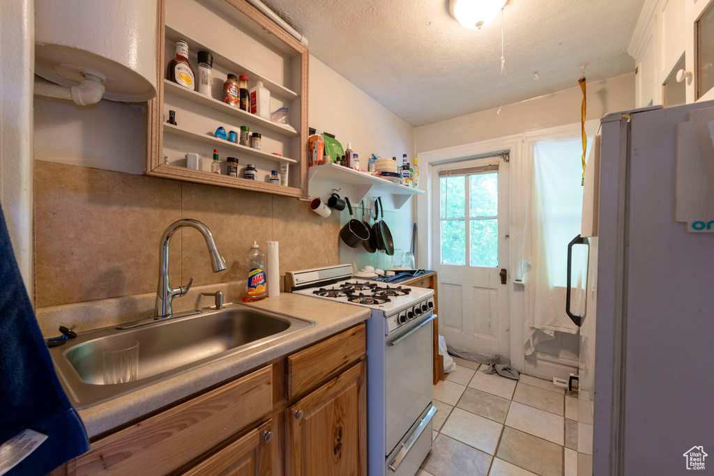 Kitchen with white appliances, a sink, tasteful backsplash, brown cabinetry, and open shelves