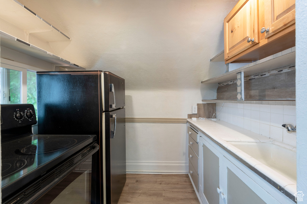 Kitchen with black electric range, light countertops, baseboards, light wood-style flooring, and backsplash