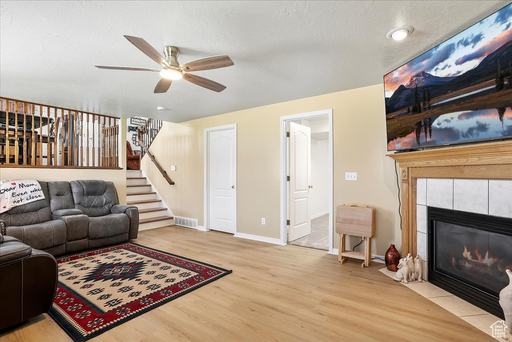 Living room featuring wood finished floors, ceiling fan, stairway, a fireplace, and a textured ceiling