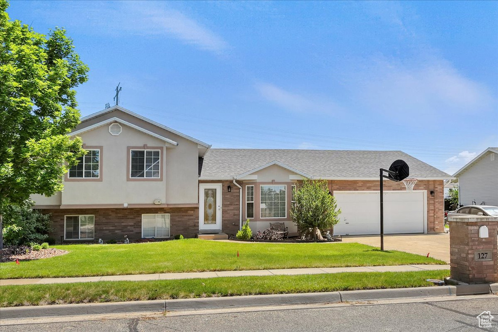 Split level home with a garage, a front lawn, concrete driveway, stucco siding, and brick siding