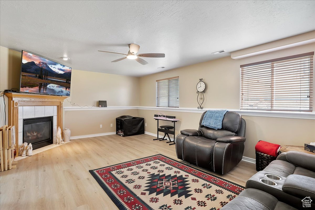 Living area with a ceiling fan, wood finished floors, a tile fireplace, baseboards, and a textured ceiling