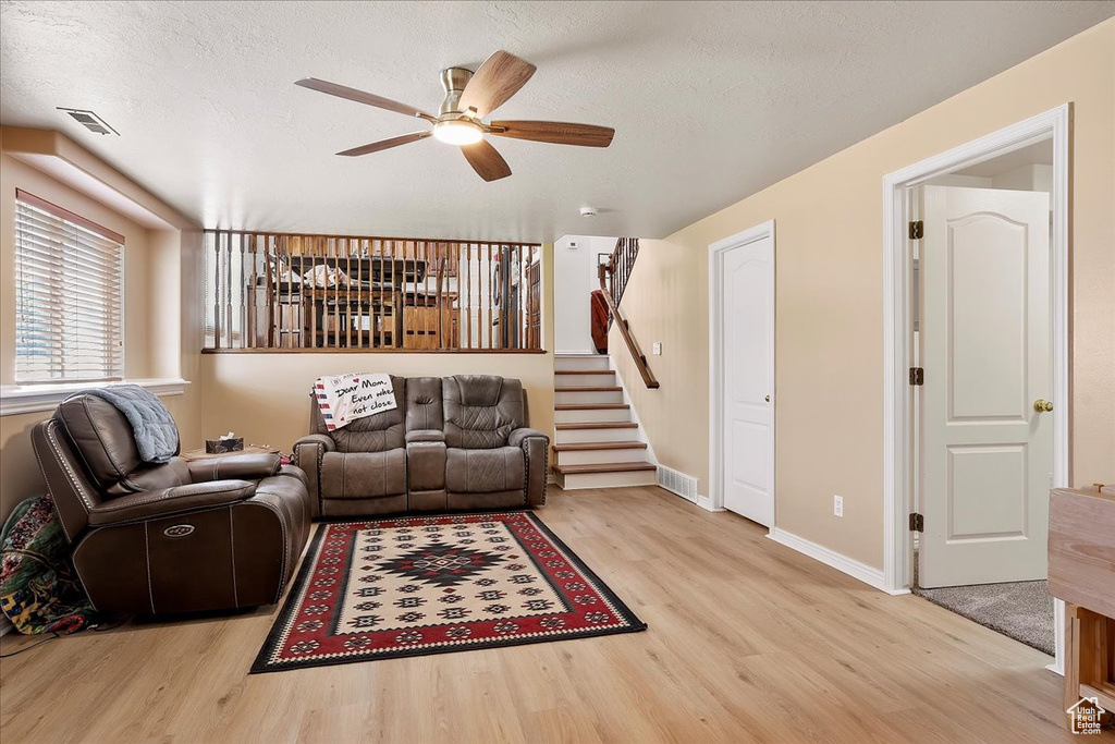 Living room featuring wood finished floors, ceiling fan, stairway, baseboards, and a textured ceiling