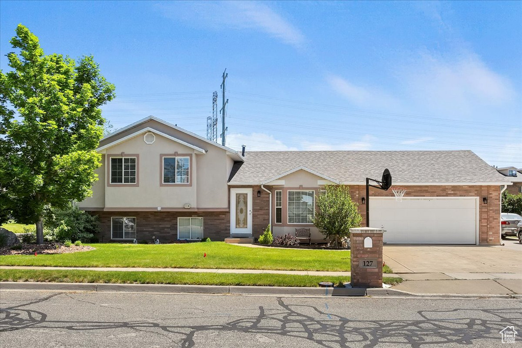 Tri-level home with concrete driveway, a garage, a front lawn, stucco siding, and brick siding