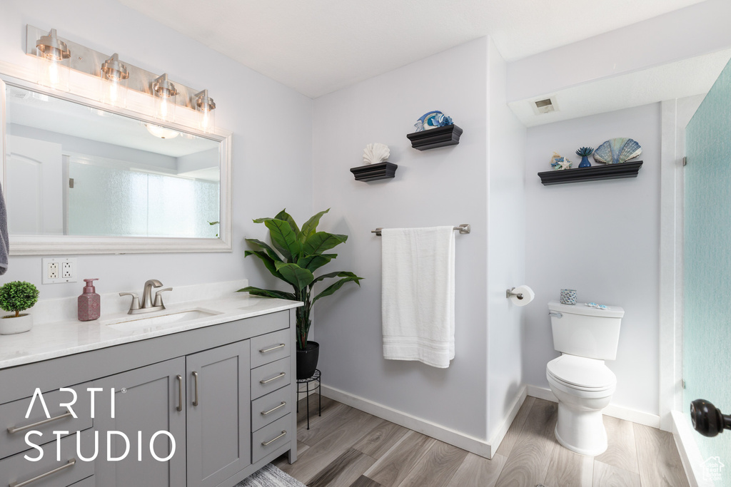 Full bath with wood finished floors, vanity, toilet, a shower, and baseboards