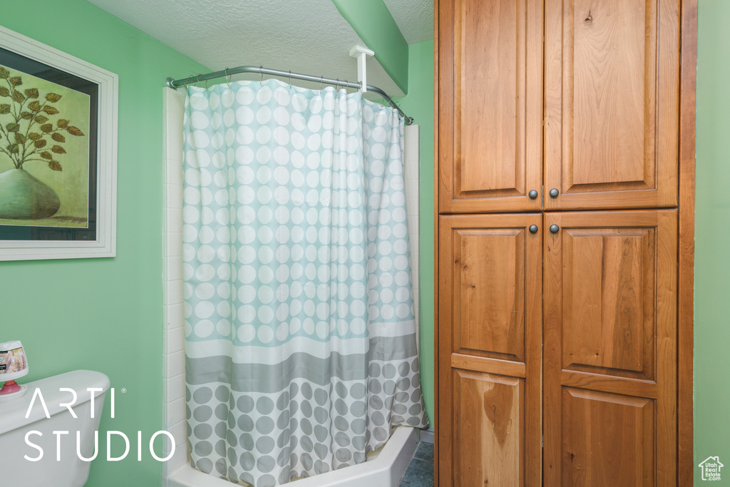 Full bath with a textured ceiling, toilet, and shower / tub combo
